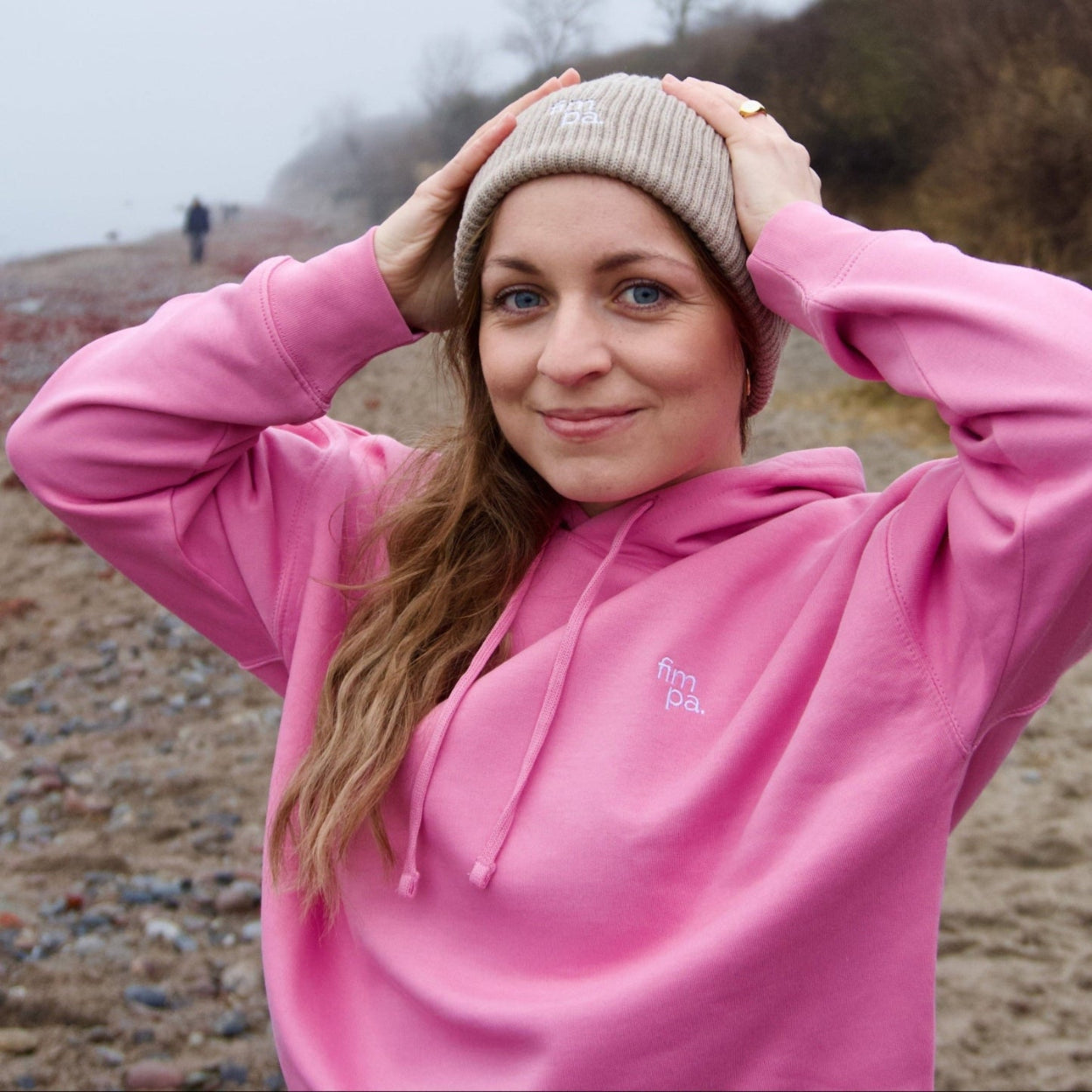Frau trägt fair produzierte Beanie in Heather Sand und genießt den windigen Tag am Strand, nachhaltige Kleidung von fimpa.de.