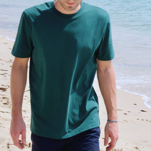 Basic T-Shirt in grün am Strand mit blauer Badehose kombiniert.