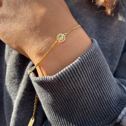 Filigranes 18 Karat vergoldetes Smile-Armband im Fokus mit einem dunkelgrauen Vintage Pullover kombiniert bei Sonnenschein.