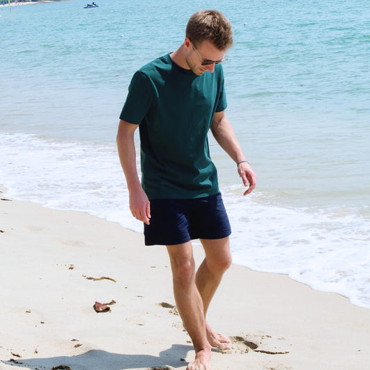 Glazed Green Unisex T-Shirt am Strand getragen mit blauer Badehose.