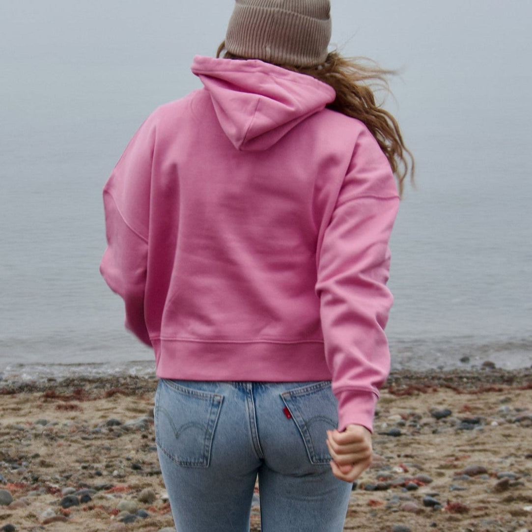 Rückansicht eines nachhaltigen Hoodies in Rosa, kombiniert mit Jeans, fotografiert am Strand für fimpa.de.