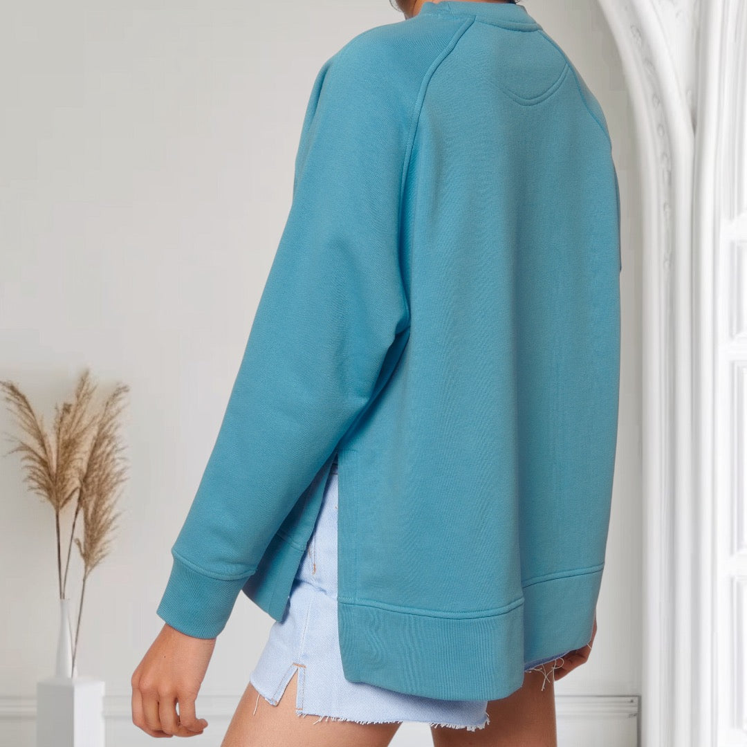 Oversized-Pullover in Blau mit Side Cut aus Bio-Baumwolle und recyceltem Polyester, dezentem weißen Sticklogo auf der Brust – nachhaltiger Streetwear-Look.