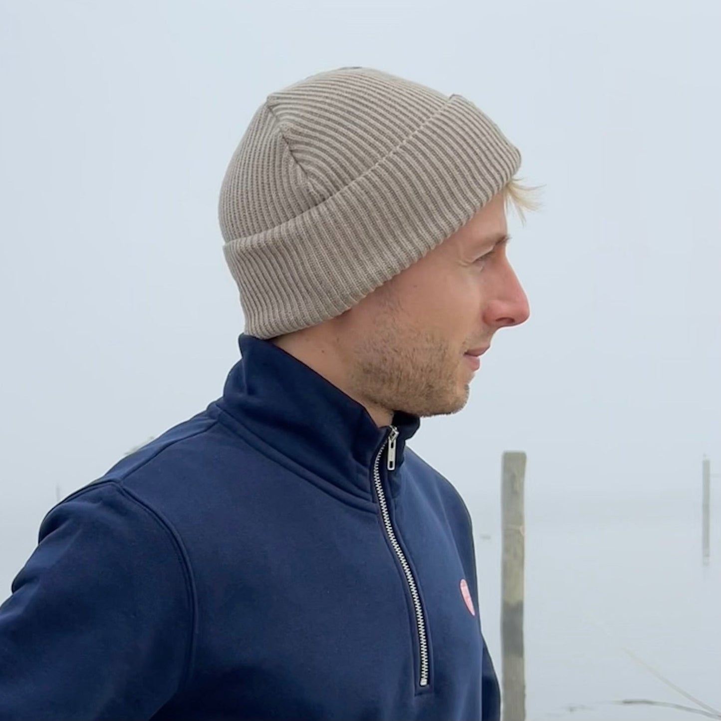 Zeitlose beigefarbene Beanie getragen bei Nebel und mit blauem Zipper Hoodie kombiniert.