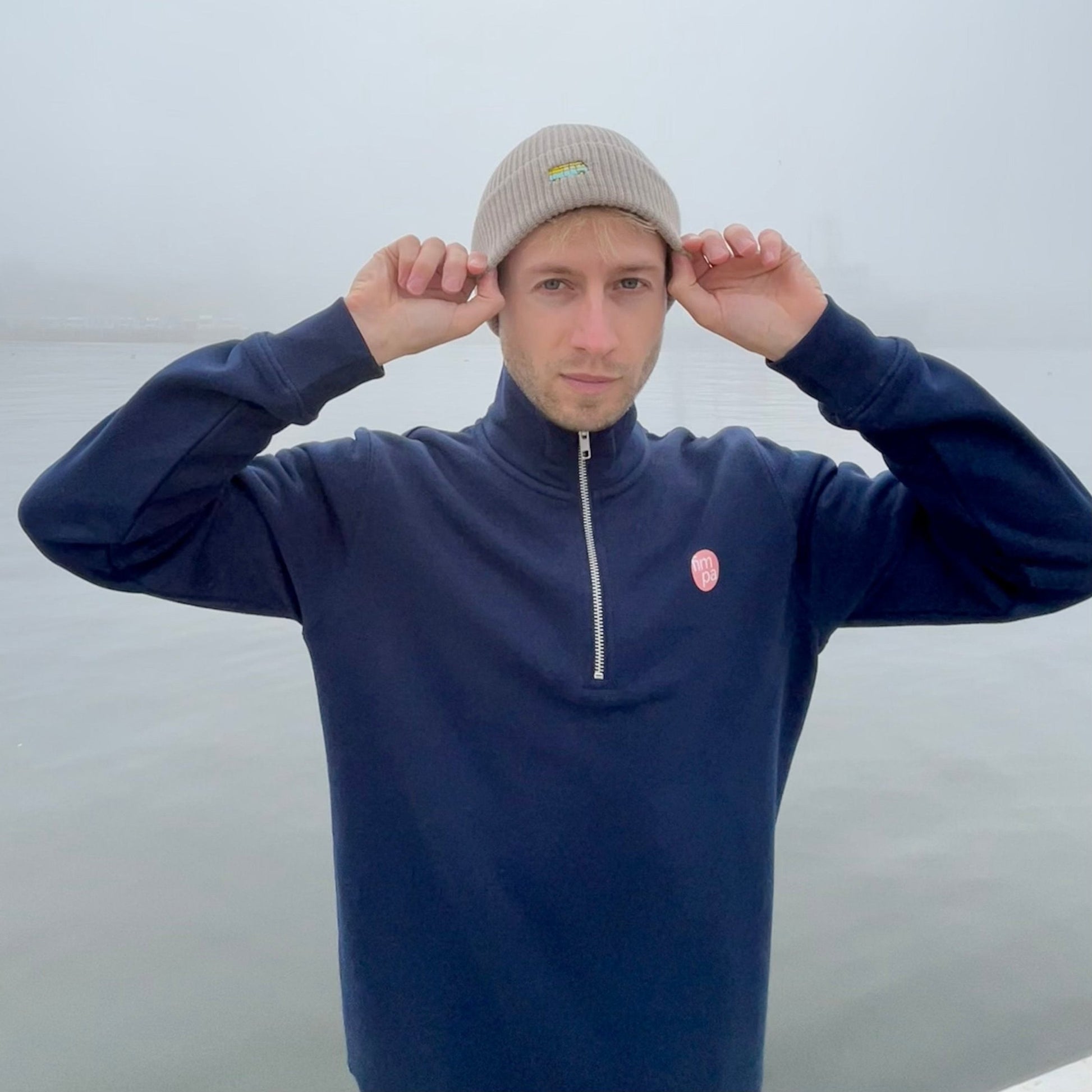 Fisherman Beanie in beige mit gesticktem Bus mit einem navyfarbenen Zipper kombiniert und im dichten Nebel getragen.